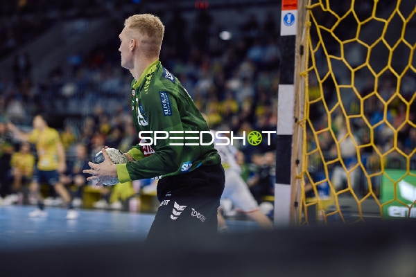 Ein Torwart von SC Magdeburg mit grünem Trikot hält den Ball und steht bereit, um das Spiel fortzusetzen.