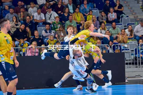 Ein Spieler der Rhein Neckar Löwen in gelbem Trikot springt dynamisch, um einen Wurf gegen HC Erlangen in weißen Trikots auszuführen.