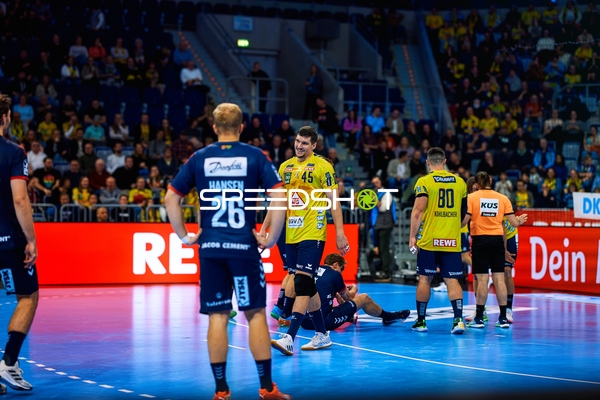 Ein Spieler von Rhein Neckar Löwen steht, während ein anderer Spieler auf dem Boden liegt.