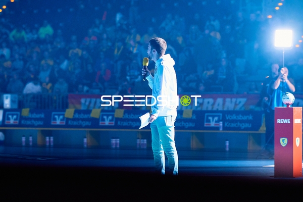 Moderator spricht mit einem Mikrofon in der Arena.