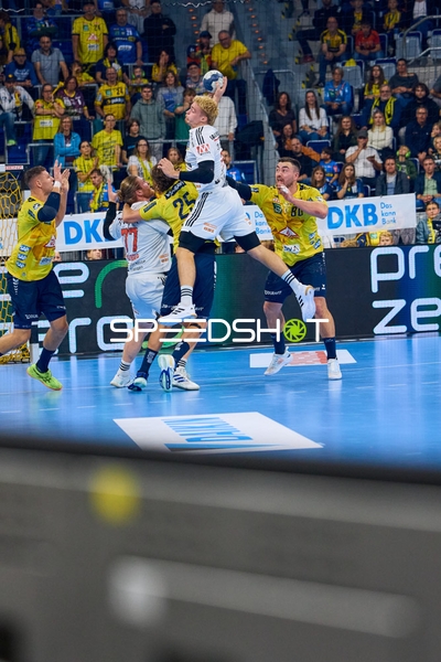 Ein Spieler von HC Erlangen springt hoch, um einen Wurf auszuführen, während er von zwei Spielern der Rhein Neckar Löwen verteidigt wird.