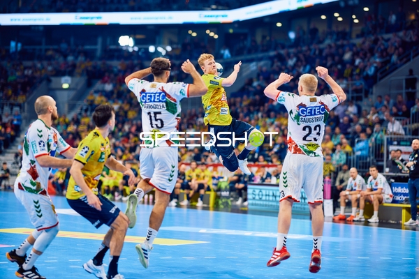 Ein Spieler der Rhein Neckar Löwen springt zum Wurf, während zwei Spieler von SC Magdeburg verteidigen.