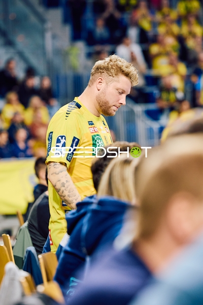 Eine Person im gelben Trikot, möglicherweise ein Spieler oder Betreuer, geht an Zuschauern vorbei.