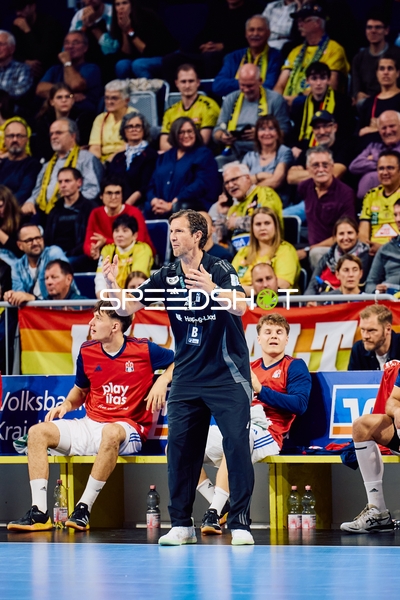 Ein Coach von HSV Hamburg gibt aktive Anweisungen von der Seitenlinie, während Spieler auf der Bank sitzen.