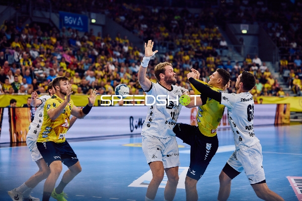 Ein Spieler der Rhein Neckar Löwen versucht den Ball zu passen oder zu werfen, während zwei Spieler von THW Kiel verteidigen.