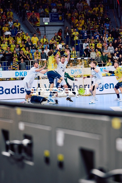 Ein Rhein Neckar Löwen-Spieler springt, um den Ball zu werfen, während mehrere HSV Hamburg-Verteidiger versuchen, den Wurf zu blockieren.