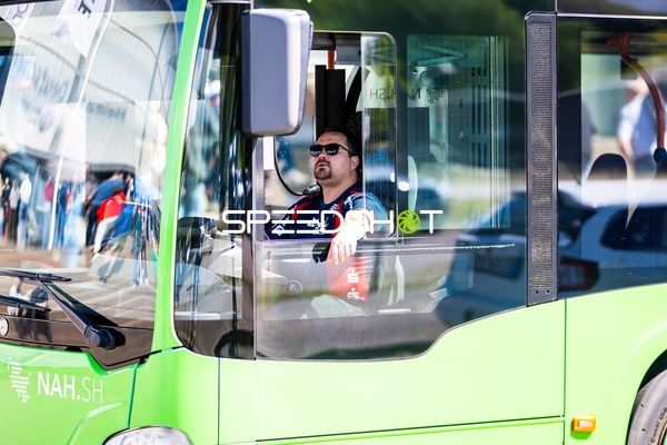 Ein Mann sitzt im Fahrerhaus eines grünen Busses mit Sonnenbrille und trägt ein Flensburg Trikot