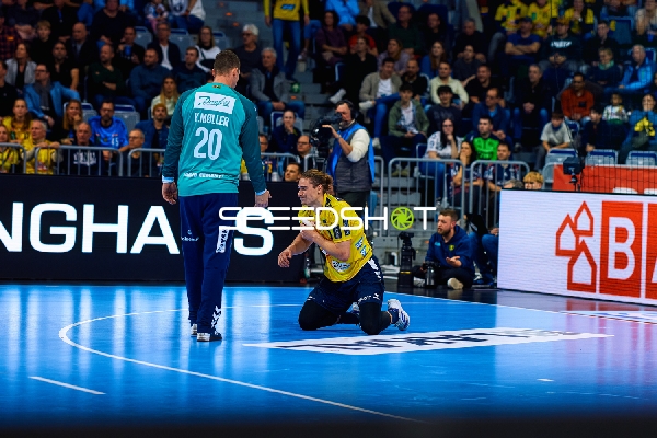 Ein Spieler von Rhein Neckar Löwen ist kniend auf dem Spielfeld, während ein Spieler von SG Flensburg Handewitt sich ihm nähert.