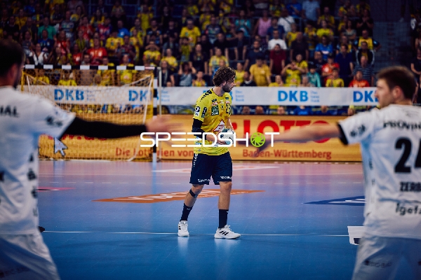 Ein Spieler von Rhein Neckar Löwen mit der Nummer 3 hält den Ball in der Mitte des Spielfelds, während Spieler von THW Kiel versuchen, ihn zu blockieren.