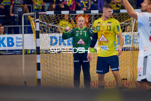 Ein Spieler der Rhein Neckar Löwen in gelbem Trikot hebt die Arme vor dem Tor, während der Torhüter verteidigt.