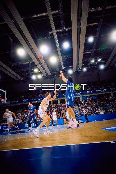 Ein Spieler von Brose Bamberg wirft einen Ball, während ein Gegenspieler versucht zu blocken.