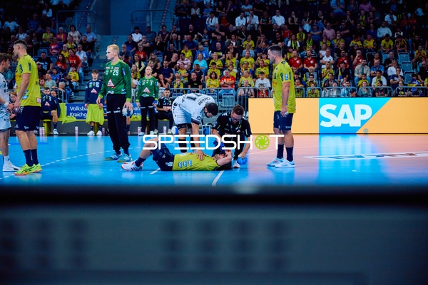 Ein Spieler von Rhein Neckar Löwen liegt verletzt auf dem Spielfeld, während andere Spieler und Betreuer sich um ihn kümmern.