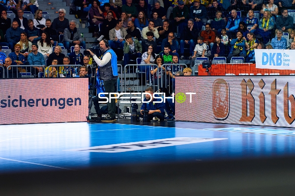 Das Bild zeigt das Spielfeld und die Zuschauertribüne während eines Handballspiels.