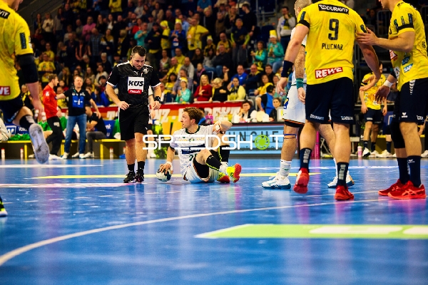 Ein Spieler von HSG Wetzlar sitzt auf dem Boden, während Spieler von Rhein Neckar Löwen und ein Schiedsrichter danebenstehen.