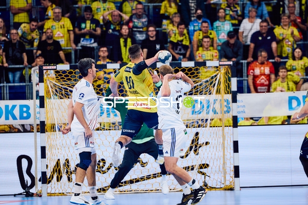 Ein Spieler der Rhein Neckar Löwen im gelben Trikot wirft den Ball Richtung Tor, während ein Spieler der HSV Hamburg in der Verteidigung aktiv ist.