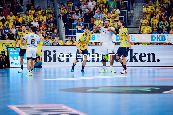 Ein Spieler von MT Melsungen in weißem Trikot mit der Nummer 6 ist im Zweikampf mit einem Spieler von Rhein Neckar Löwen in gelbem Trikot auf der Spielfläche.