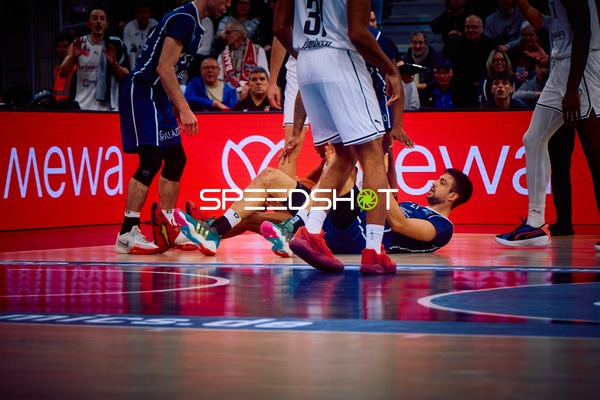 Ein Spieler von MLP Academics Heidelberg sitzt am Boden, während ein Spieler von Brose Bamberg daneben steht.