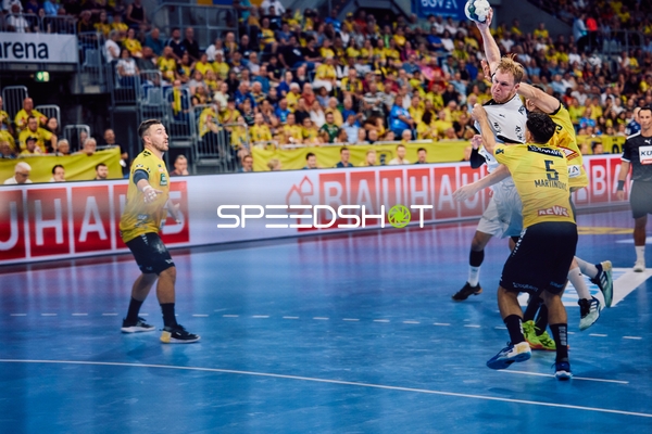 Ein Spieler von THW Kiel springt zum Wurf, während zwei Spieler von Rhein Neckar Löwen verteidigen.