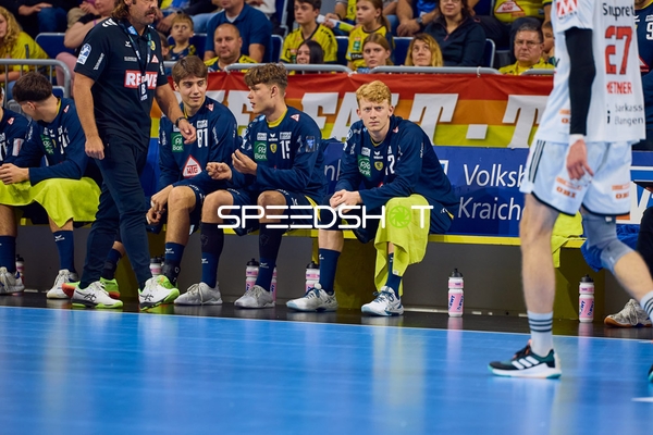 Jon Lindenchrone Andersen und Arnór Snaer Óskarsson sitzen mit ihren Teamkollegen der Rhein Neckar Löwen auf der Bank, während Antonio Metzner vom HC Erlangen vorbeiläuft.