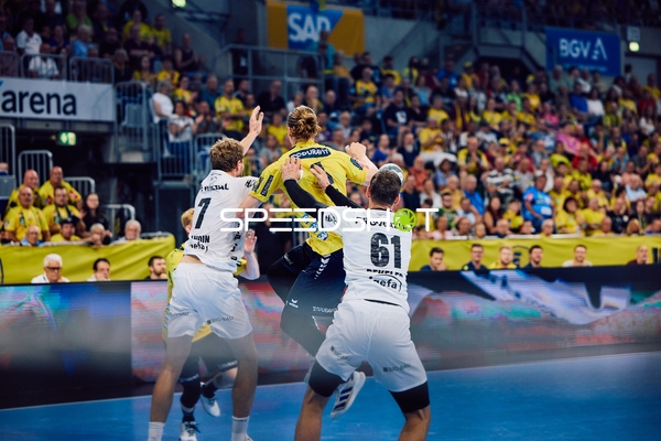 Ein Spieler der Rhein Neckar Löwen springt für einen Wurf, während zwei Spieler von THW Kiel verteidigen.