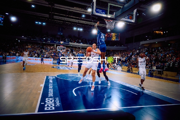 Ein Spieler von MLP Academics Heidelberg versucht einen Korbleger, während ein Spieler von Brose Bamberg einen Block versucht.