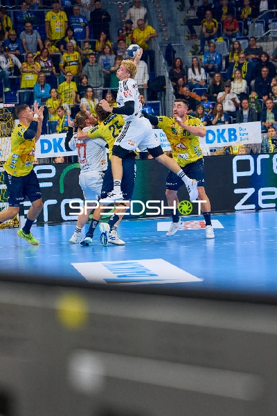 Ein Spieler von THW Kiel springt in die Luft, um den Ball zu werfen, während Rhein Neckar Löwen Spieler versuchen zu blocken.