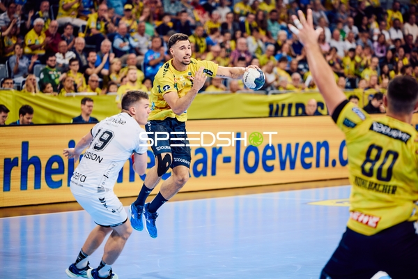 Ein Spieler von Rhein Neckar Löwen im gelben Trikot springt zum Wurf, während ein Spieler von MT Melsungen versucht zu verteidigen.