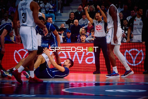 Ein Spieler von Brose Bamberg liegt auf dem Boden, während andere Spieler um ihn herum stehen.