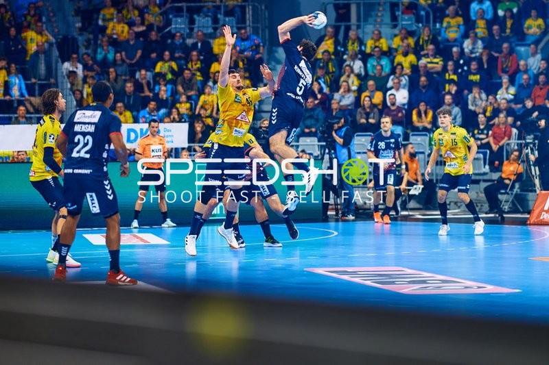 Ein Spieler von SG Flensburg Handewitt springt, um einen Wurf aufs Tor zu machen, während die Verteidigung von Rhein Neckar Löwen versucht zu blocken.