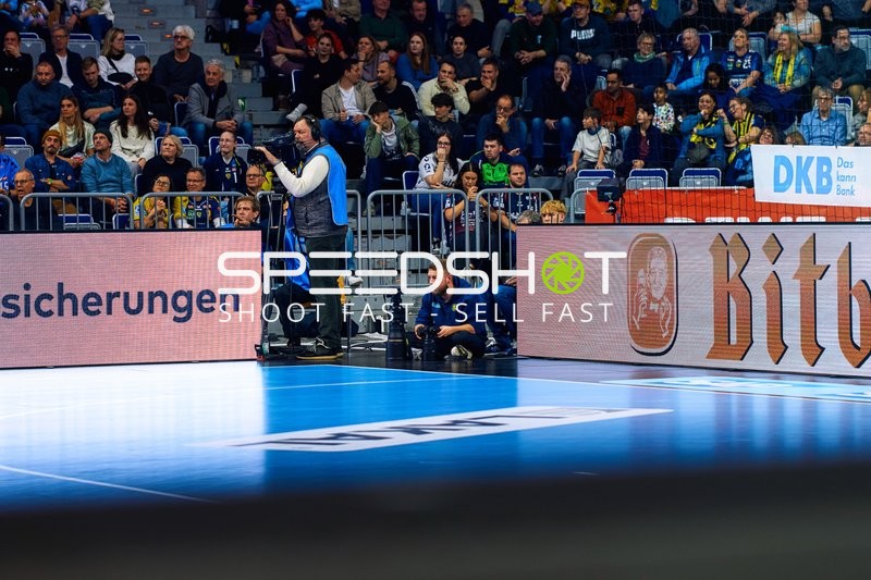 Das Bild zeigt das Spielfeld und die Zuschauertribüne während eines Handballspiels.