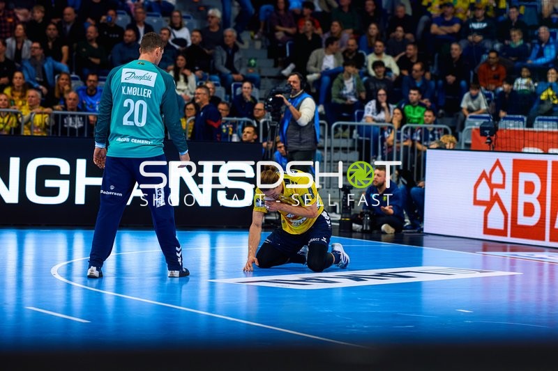 Ein Spieler der Rhein Neckar Löwen kniet auf dem Boden, während ein Spieler der SG Flensburg Handewitt daneben steht.