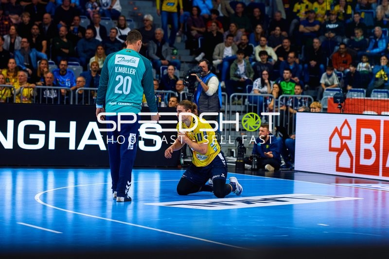 Ein Spieler von Rhein Neckar Löwen ist kniend auf dem Spielfeld, während ein Spieler von SG Flensburg Handewitt sich ihm nähert.