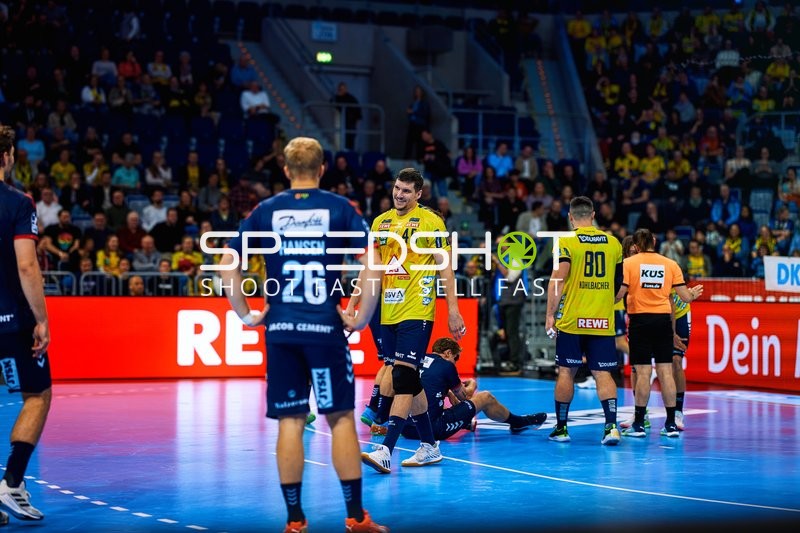 Ein Spieler von Rhein Neckar Löwen steht, während ein anderer Spieler auf dem Boden liegt.