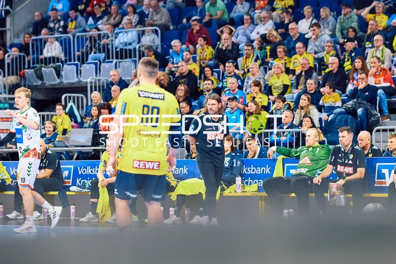 Ein Spieler der Rhein Neckar Löwen bewegt sich auf dem Spielfeld, während der Trainer Anweisungen gibt.
