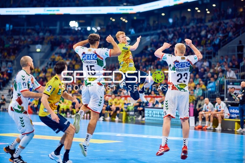 Ein Spieler der Rhein Neckar Löwen springt zum Wurf, während zwei Spieler von SC Magdeburg verteidigen.