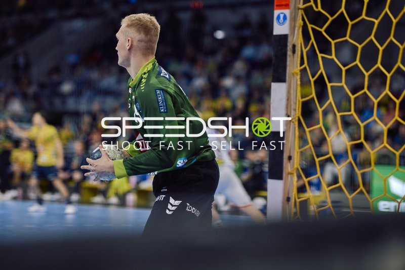 Ein Torwart von SC Magdeburg mit grünem Trikot hält den Ball und steht bereit, um das Spiel fortzusetzen.