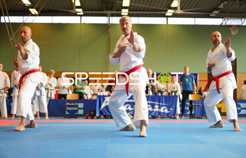 Drei Karateka mit rotem Gürtel führen synchrone Kata-Sequenz aus