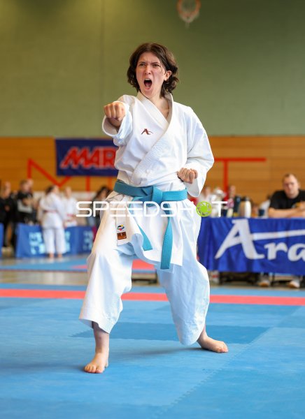 Karateka mit blauem Gürtel führt Kata-Technik mit intensivem Kiai aus