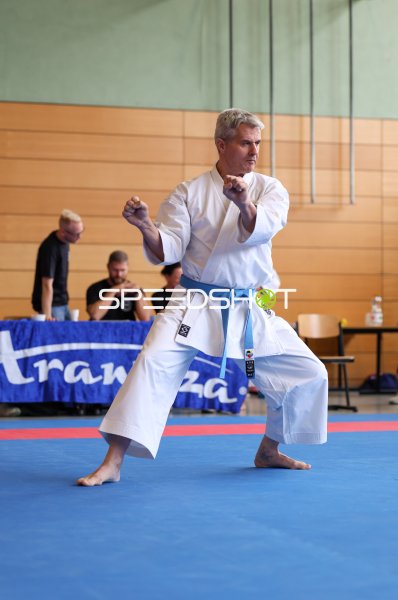 Karateka im weißen Gi führt Kata-Technik auf blauer Wettkampffläche aus