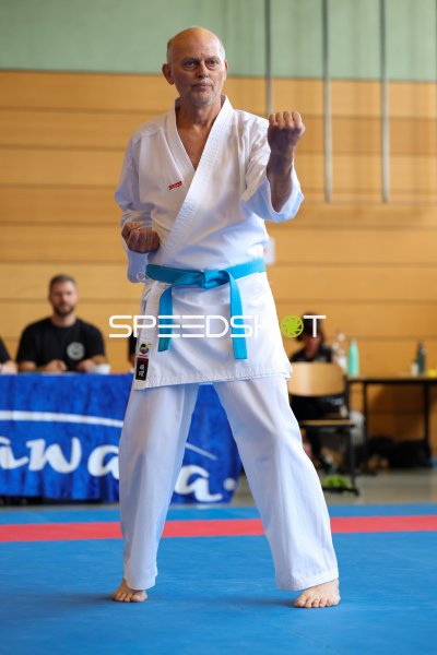 Karateka im weißen Gi führt Kata-Sequenz auf blauer Wettkampffläche aus