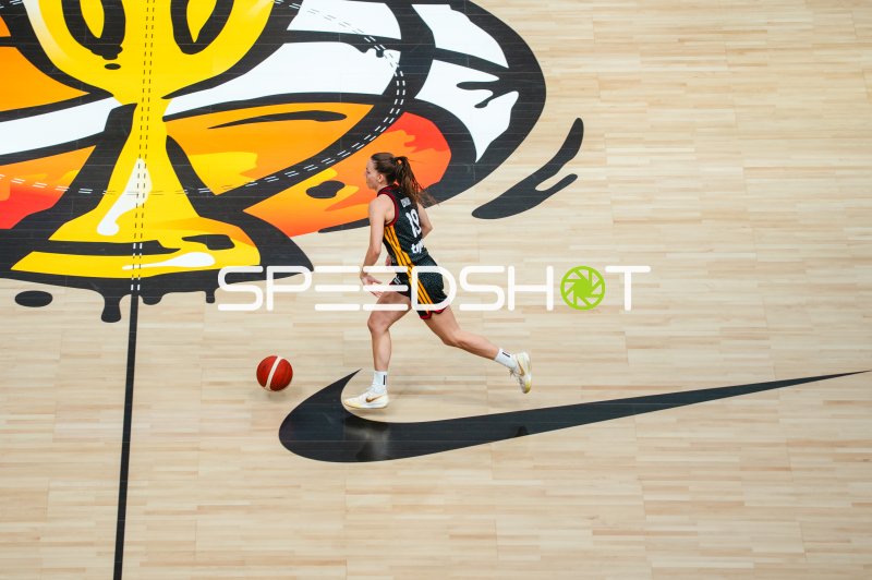 Basketballspielerin dribbelt am Ballmit vor Teamlogo auf dem Parkett