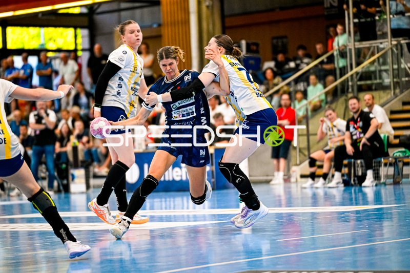 Rückraumspielerin im Dunkelblauen Trikot setzt sich gegen zwei Abwehrspielerinnen durch