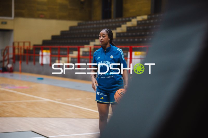 Frau im Trainingsshirt von Alba Berlin mit Basketball in der Halle