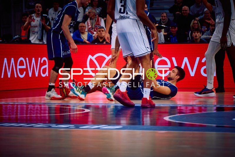 Ein Spieler von MLP Academics Heidelberg sitzt am Boden, während ein Spieler von Brose Bamberg daneben steht.