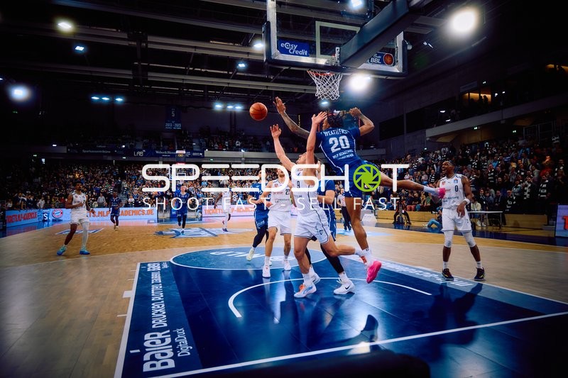 Ein Spieler von Brose Bamberg mit der Nummer 20 springt zum Korb für einen Wurf, während zwei Verteidiger von MLP Academics Heidelberg versuchen, ihn zu blocken.