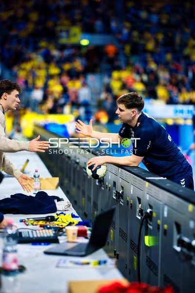 Ein Spieler im blauen Trikot interagiert mit Personen am Spielfeldrand.