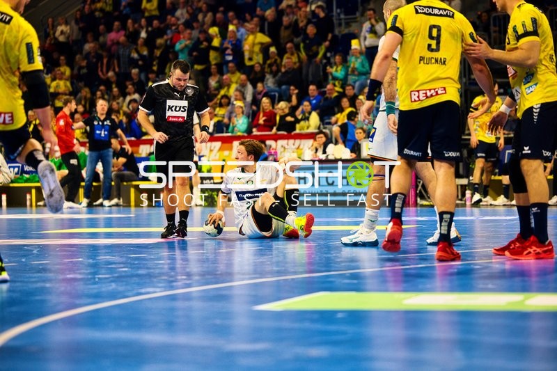 Ein Spieler von HSG Wetzlar sitzt auf dem Boden, während Spieler von Rhein Neckar Löwen und ein Schiedsrichter danebenstehen.