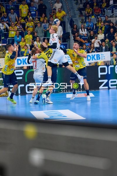 Ein Spieler von THW Kiel springt in die Luft, um den Ball zu werfen, während Rhein Neckar Löwen Spieler versuchen zu blocken.