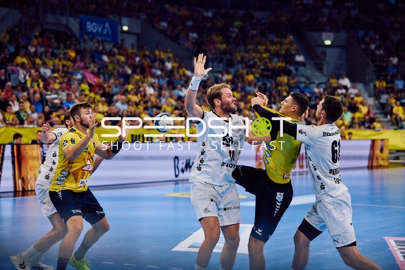 Ein Spieler der Rhein Neckar Löwen versucht den Ball zu passen oder zu werfen, während zwei Spieler von THW Kiel verteidigen.