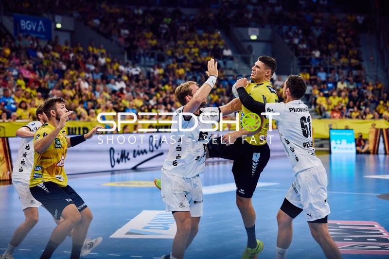 Ein Spieler der Rhein Neckar Löwen versucht, den Ball am Kreis zu werfen, während zwei Spieler von THW Kiel in der Verteidigung sind.